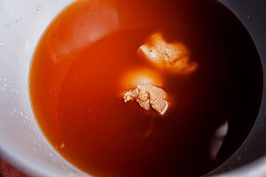 A close-up of a bowl containing reddish-brown liquid with two clumps of beige, solid matter—possibly miso pickled onions—floating on the surface.