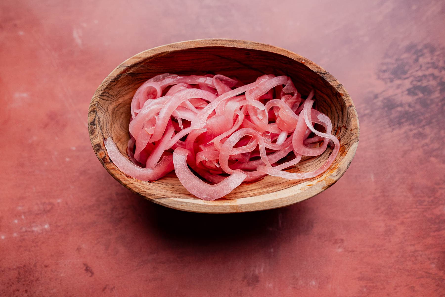 A wooden bowl filled with thinly sliced miso pickled onions on a reddish-brown surface.