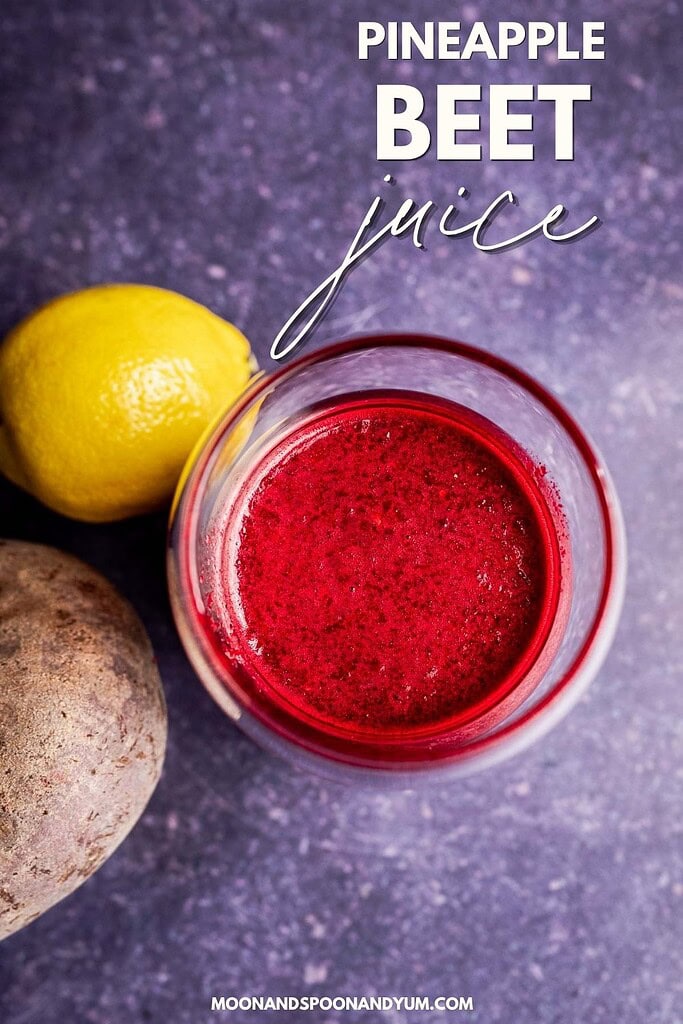 A glass of beet pineapple juice rests on a granite surface, next to a whole lemon and a beet.