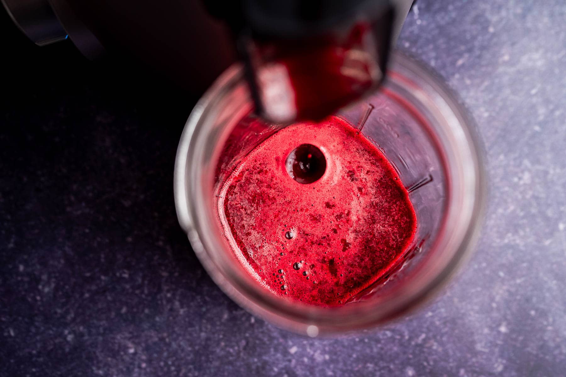 Top-down view of a glass filled with freshly made beet pineapple juice, likely from a juicer, on a dark speckled countertop.