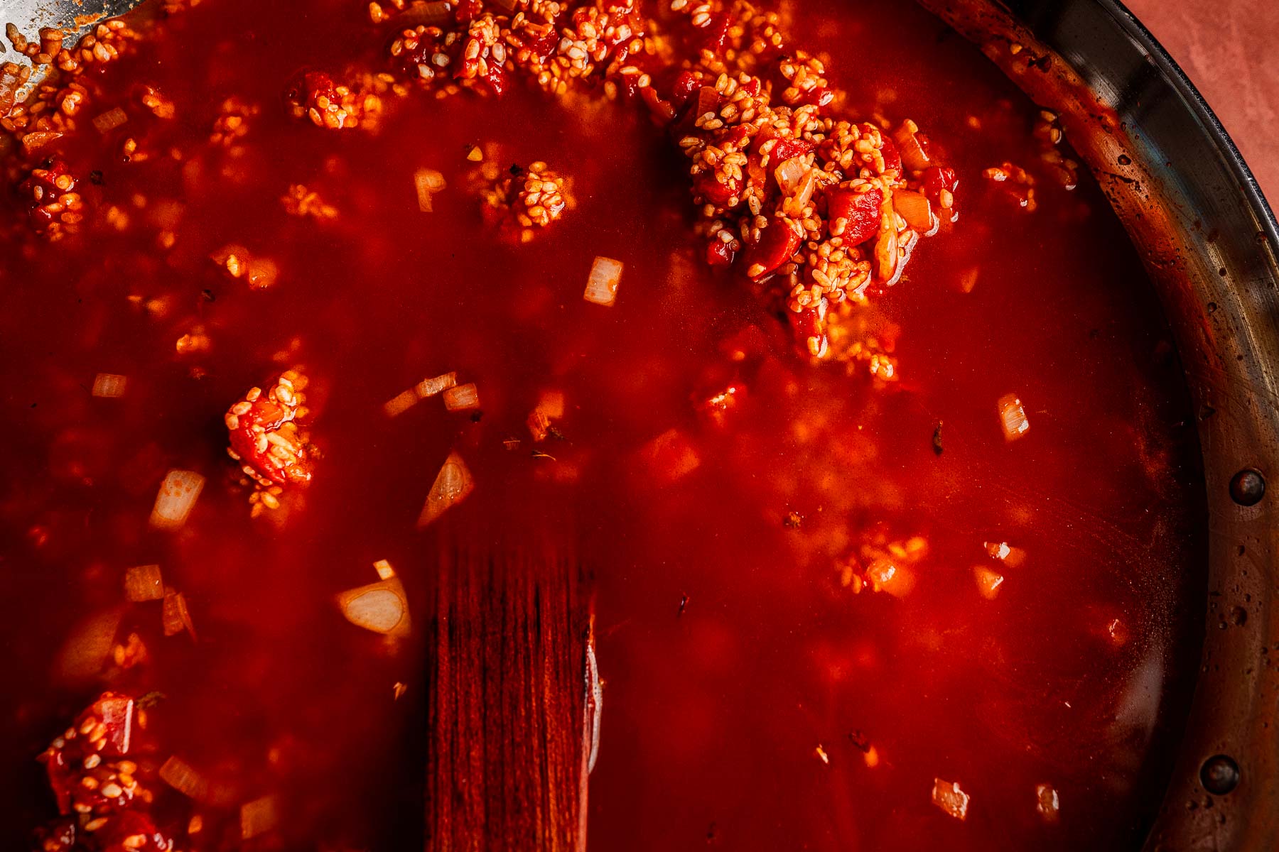 Close-up of a pot of red tomato sauce with visible diced onions and a wooden spoon partially submerged, perfect as a flavorful base for dishes like Vegetarian Paella.