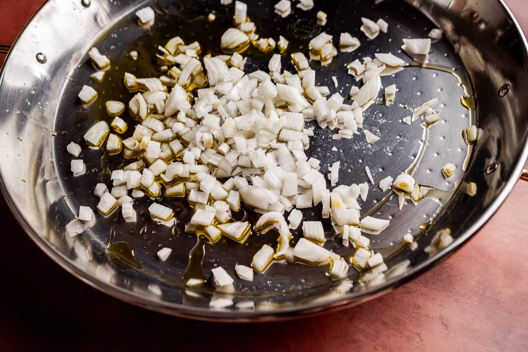 Chopped onions and olive oil in a stainless steel pan, the perfect start for a flavorful Vegetarian Paella.