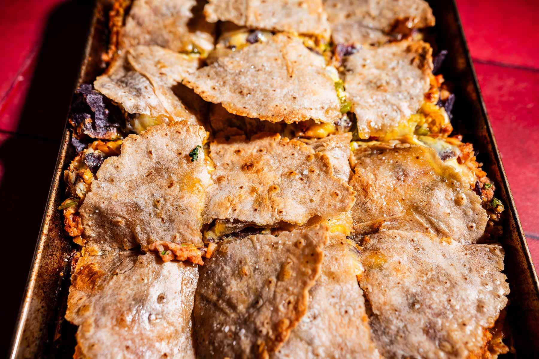 A baking tray filled with pieces of golden-brown sheet pan crunchwraps, layered with melted cheese and visible fillings.