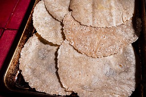 Several round, uncooked corn tortillas are stacked and overlapping on a metal baking sheet, ready to be transformed into a delicious sheet pan crunchwrap.