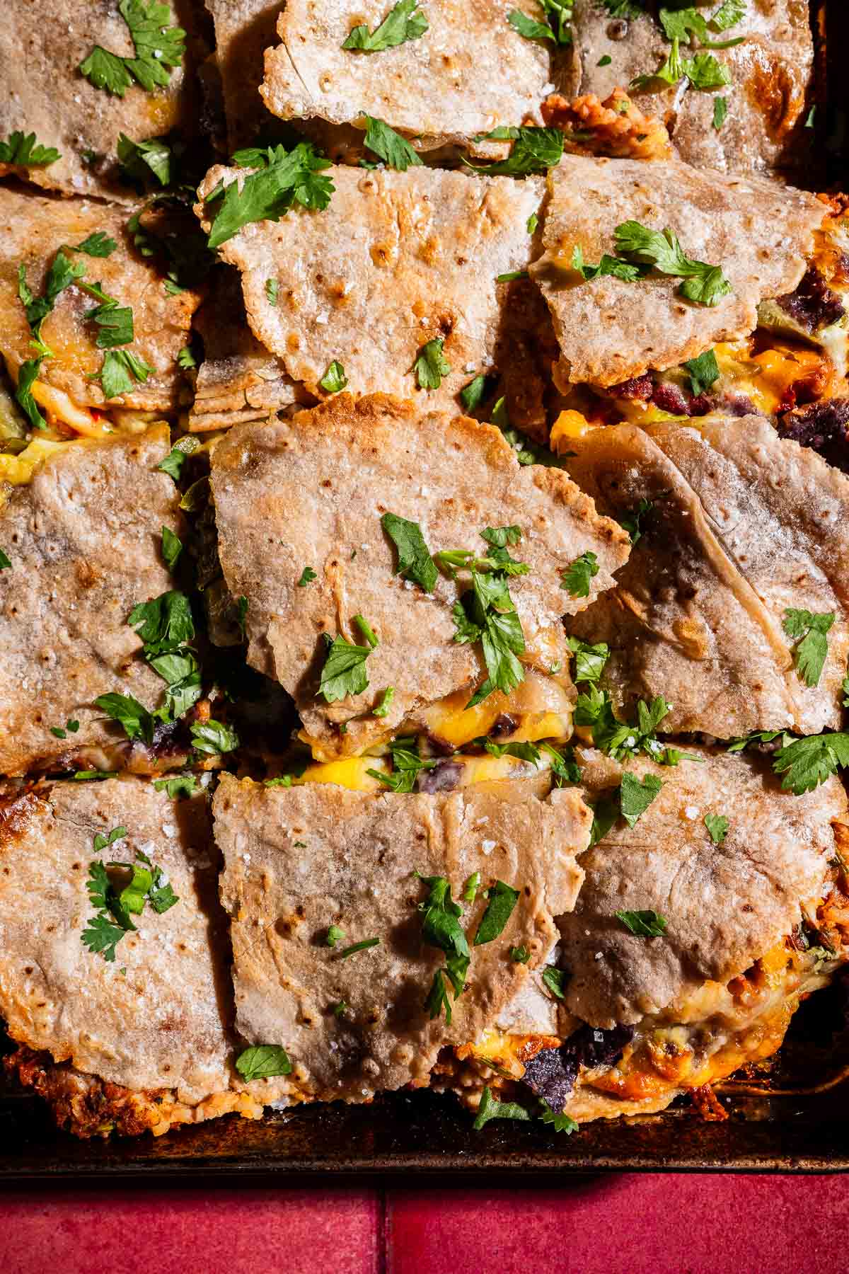 Sliced quesadillas made with whole wheat tortillas, melted cheese, and fresh cilantro on top—like a sheet pan crunchwrap for easy sharing.