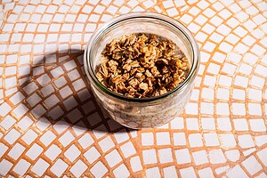 A glass jar filled with overnight oats and banana chia pudding, topped with granola, sits on a tile-patterned surface.