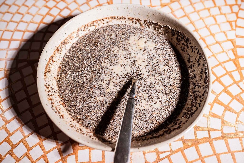 A bowl of banana chia pudding with a spoon resting inside, placed on a tiled surface.