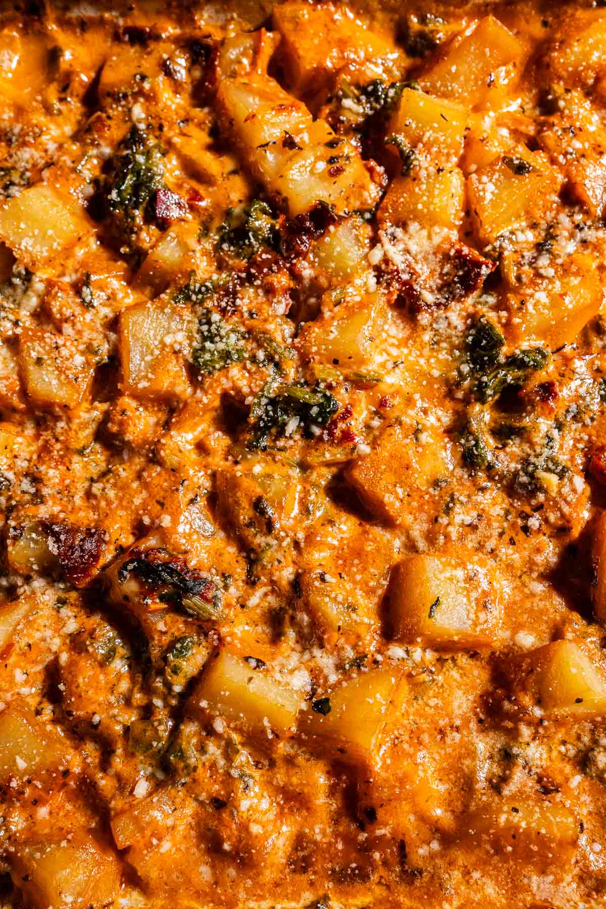 Close-up of a baked casserole featuring marry me potatoes, fresh spinach, melted cheese, and a perfectly browned, crispy surface.