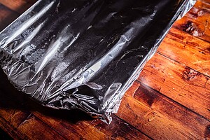 A rectangular baking dish covered with aluminum foil sits on a wooden surface, ready to reveal a batch of delicious marry me potatoes.