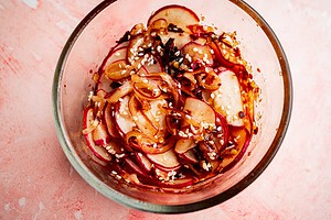 Thinly sliced radishes tossed with sesame seeds and seasoning create a vibrant spicy radish recipe, beautifully arranged in a glass bowl and photographed from above on a pink surface.