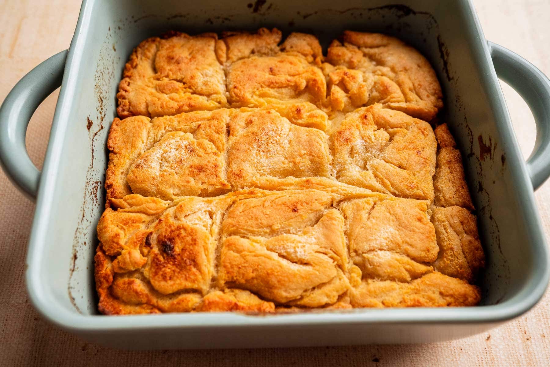 A square baking dish filled with golden brown, flaky gluten free butter swim biscuits, divided into nine pieces, rests on a light-colored surface.