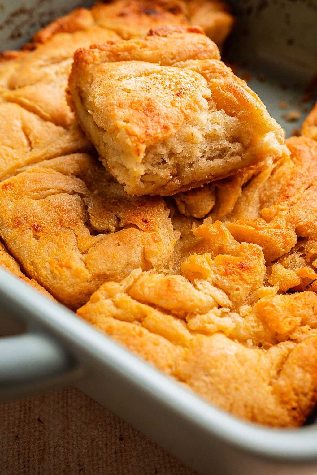 Close-up of golden, flaky gluten free butter swim biscuits in a baking dish, with one biscuit broken in half to reveal its soft interior.