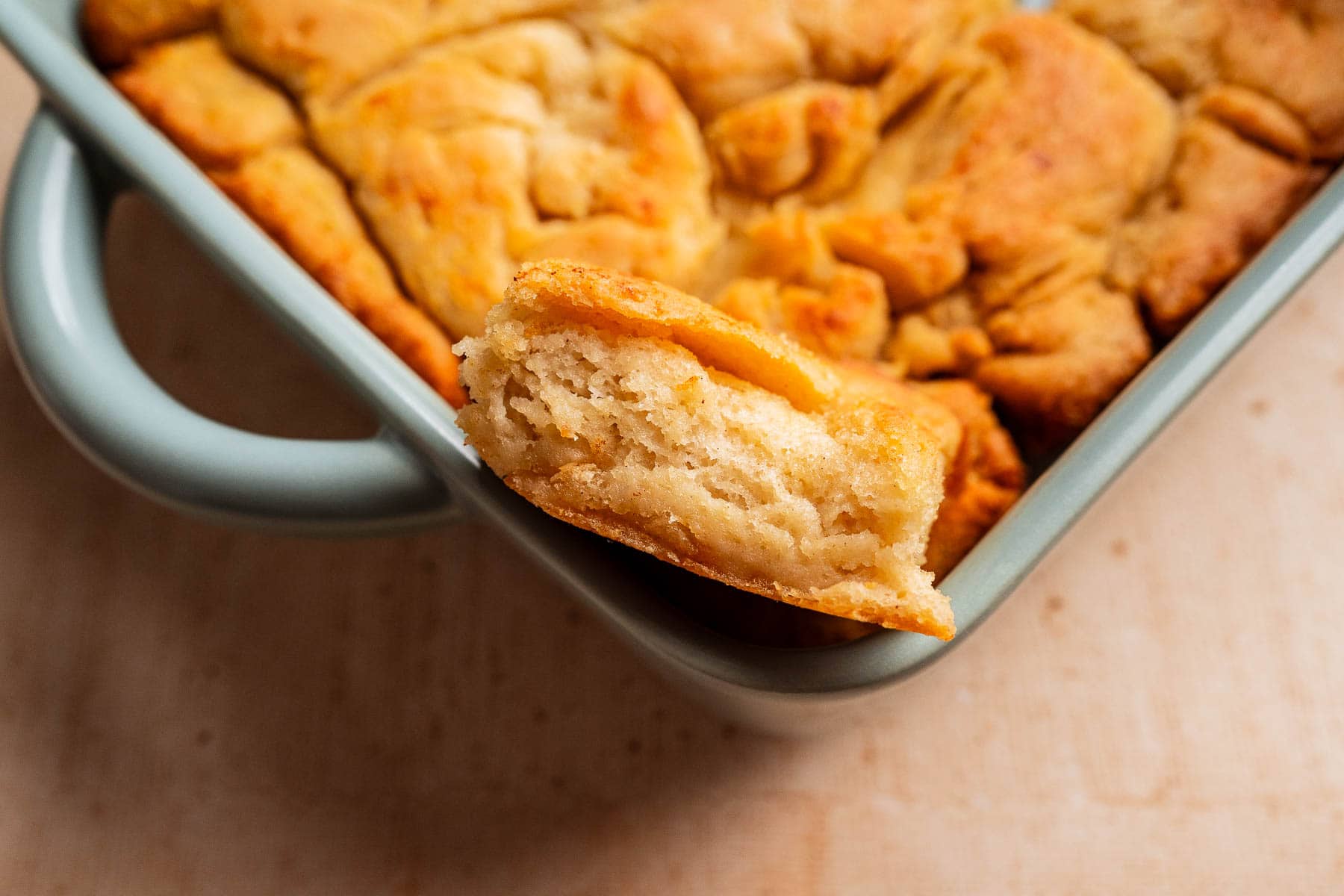 A close-up of a baking dish filled with golden, flaky gluten free butter swim biscuits, with one piece resting on the edge showing its beautifully layered interior.