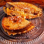 A kimchi grilled cheese sandwich with melted cheese is cut in half and served on a clear glass plate.