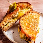 Jalapeno popper grilled cheese sandwich with melted cheese and jalapeño slices, cut in half and served on a white plate, one half secured with a toothpick.