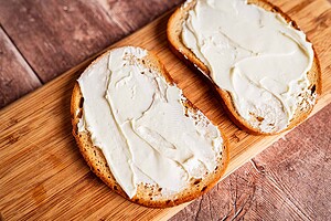 Two slices of bread with cream cheese spread on top, perfect for making a delicious jalapeno popper grilled cheese, placed on a wooden cutting board.