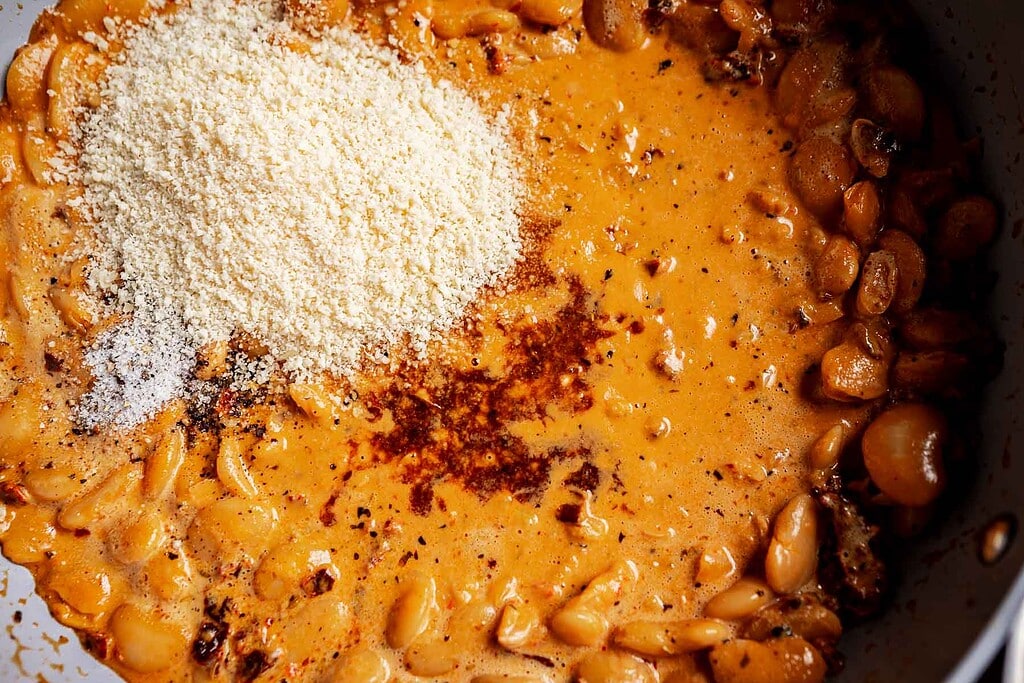 Cooked pasta shells in a creamy orange sauce with marry me butter beans, topped with grated Parmesan cheese and seasonings.