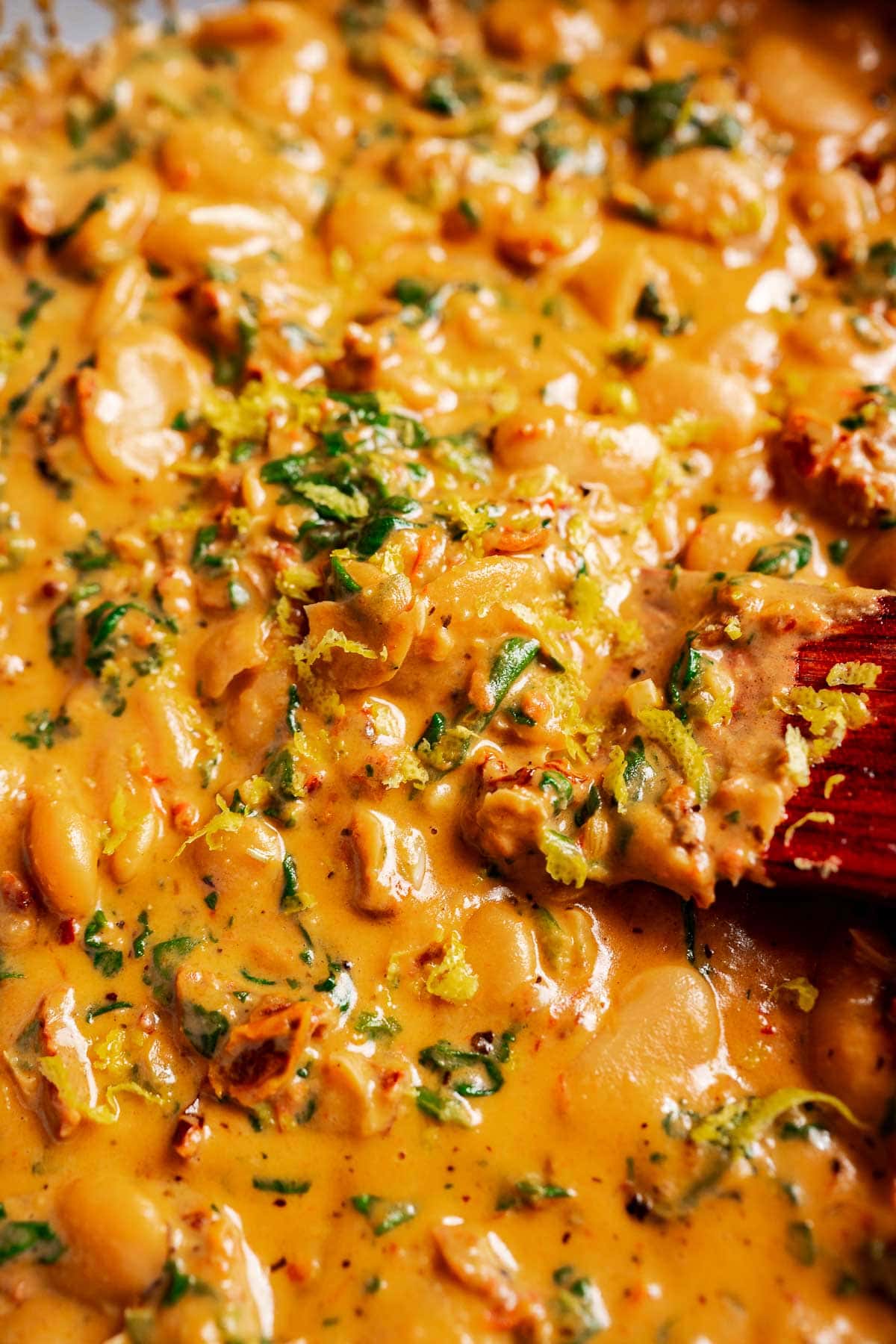 A creamy Mary Mee stew of butter beans, chopped herbs, visible lemon zest and chunks of sun-dried tomatoes stirred with a wooden spoon.