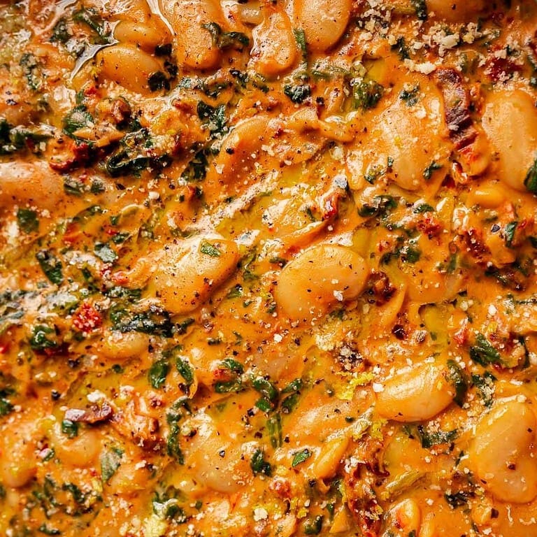 Close-up of creamy "marry me butter beans" in a rich tomato sauce with herbs and spices, topped with grated cheese and cracked black pepper.