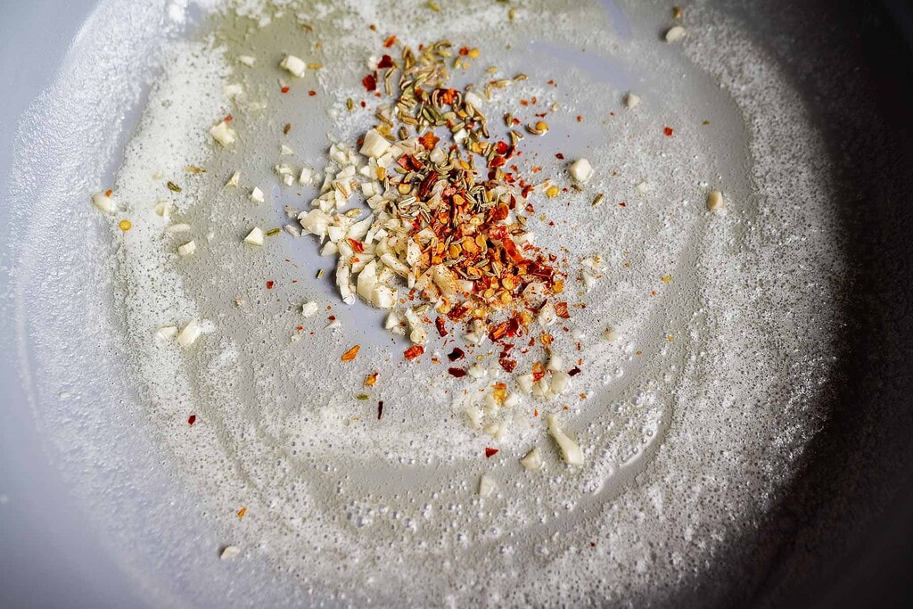 Minced garlic, red pepper flakes, and herbs are sautéing in melted butter in a pan, creating the perfect base for marry me butter beans.