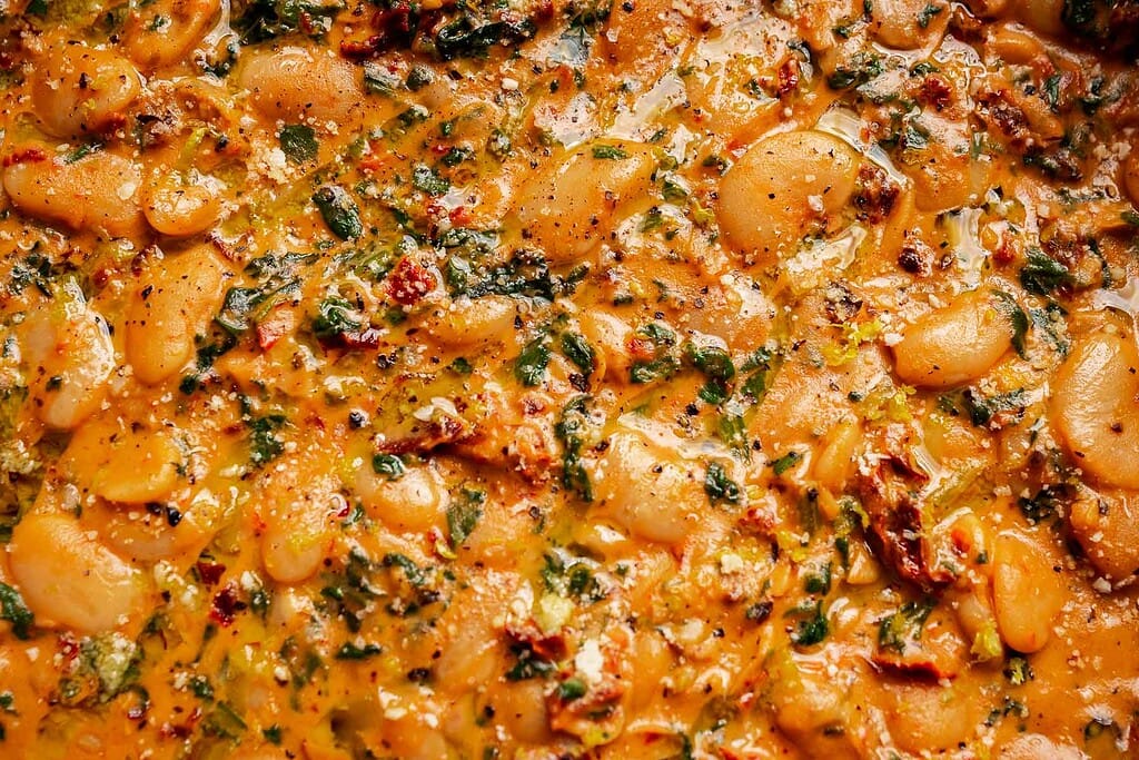 Close-up of a cooked dish featuring marry me butter beans, herbs, and a tomato-based sauce with visible spices and leafy greens.