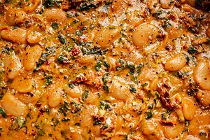 Close-up of a cooked dish featuring marry me butter beans, herbs, and a tomato-based sauce with visible spices and leafy greens.