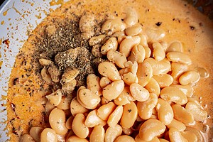 Close-up of large white marry me butter beans in a creamy orange sauce, topped with dried herbs and seasoning.