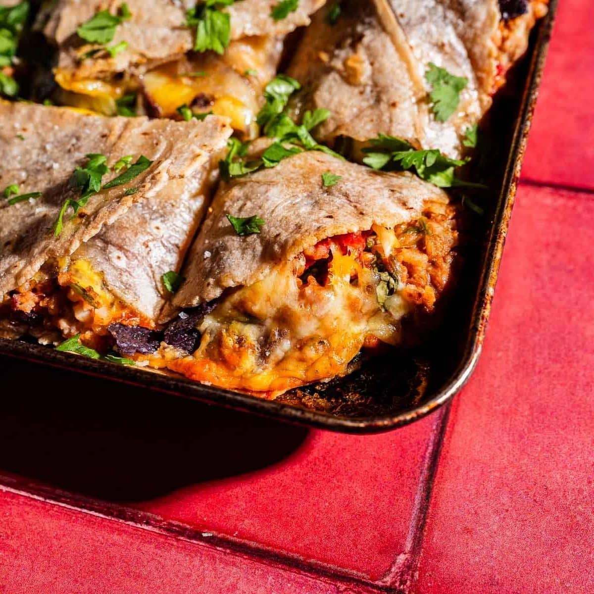 A baking tray with sliced, baked sheet pan crunchwrap quesadillas filled with vegetables and melted cheese, garnished with chopped parsley, on a red tiled surface.