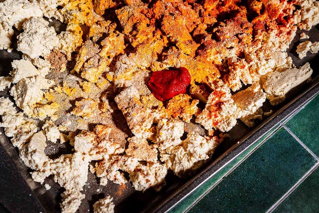 Crumbled tofu shawarma on a baking tray topped with various spices and a dollop of tomato paste.