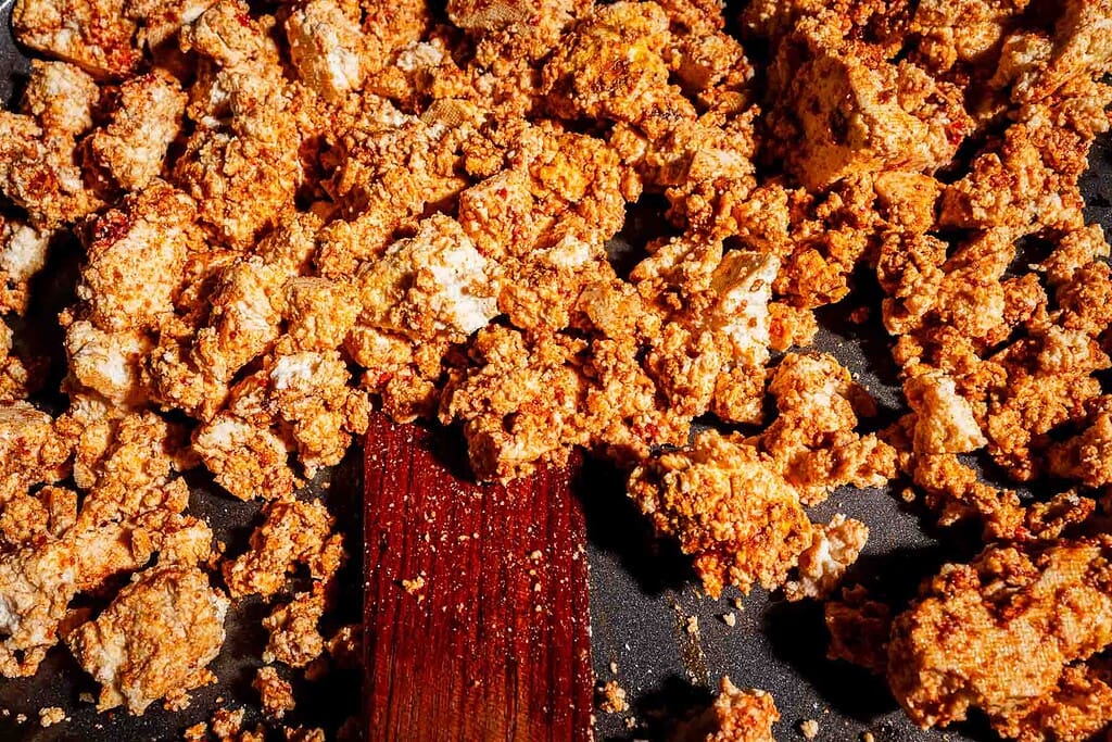 Crumbled tofu shawarma coated in spices cooking in a pan with a wooden spatula.