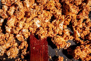 Crumbled tofu shawarma coated in spices cooking in a pan with a wooden spatula.