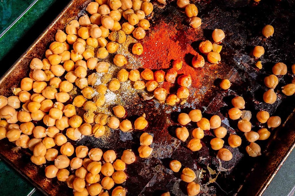 A baking sheet with scattered chickpeas, spices, and tofu shawarma seasoning, ready to be mixed and roasted.