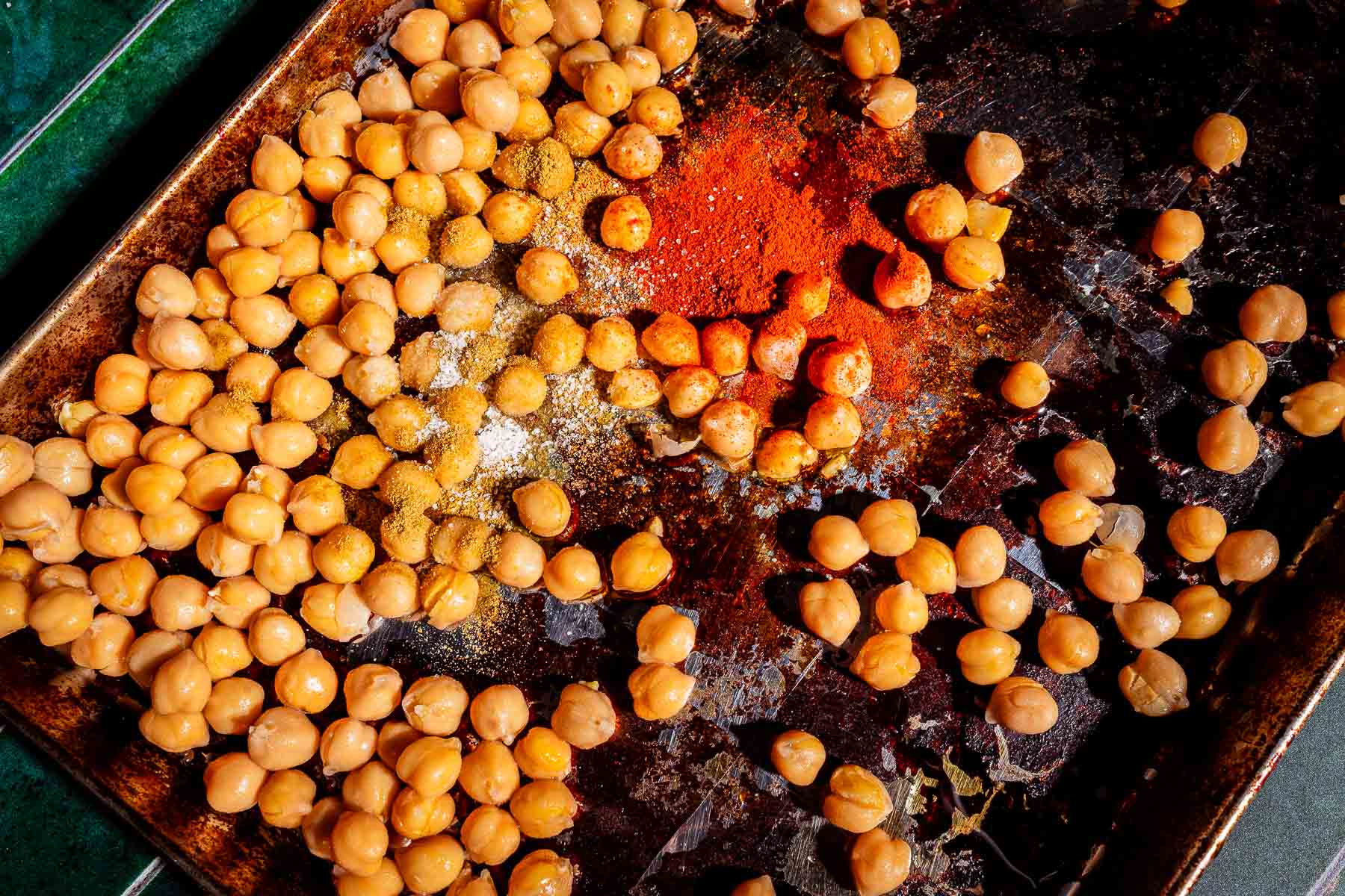 A baking sheet with scattered chickpeas, spices, and tofu shawarma seasoning, ready to be mixed and roasted.