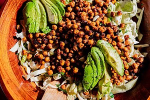 A wooden bowl filled with shredded cabbage, sliced avocado, and roasted chickpeas, tossed together for a flavorful hot honey salad.