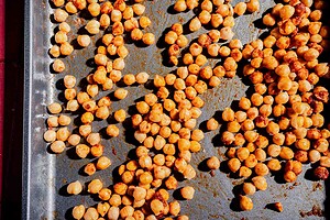 Roasted chickpeas scattered on a metal baking sheet, some with visible seasoning—perfect for tossing into a hot honey salad.