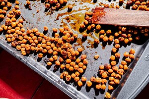 Seasoned roasted chickpeas scattered on a baking sheet, perfect for adding crunch and flavor to your next hot honey salad, with a wooden spatula resting on the edge.
