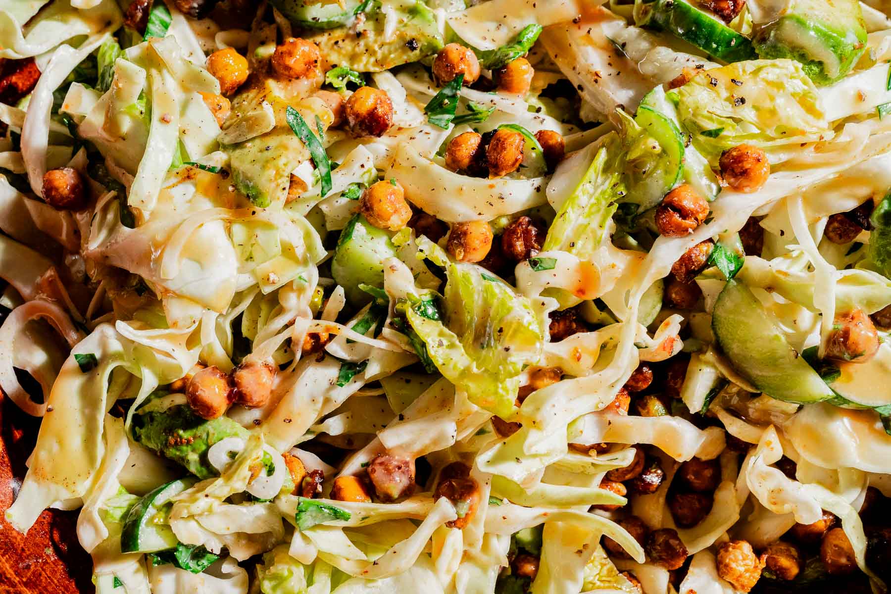 Shredded cabbage salad with avocado slices, crispy chickpeas, fresh herbs, and a light hot honey salad dressing.
