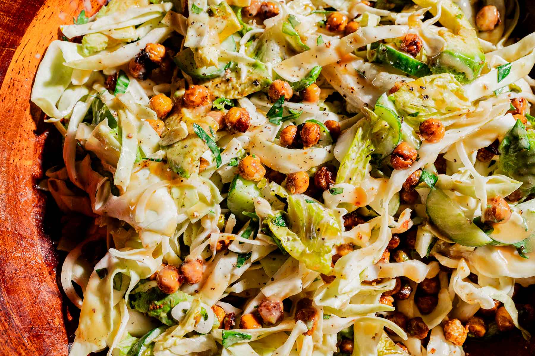Shredded cabbage salad with sliced cucumbers, crispy chickpeas, herbs, and a creamy hot honey salad dressing served in a wooden bowl.