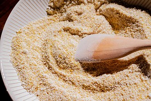 A wooden spoon resting in a bowl filled with dry yellow cornmeal.