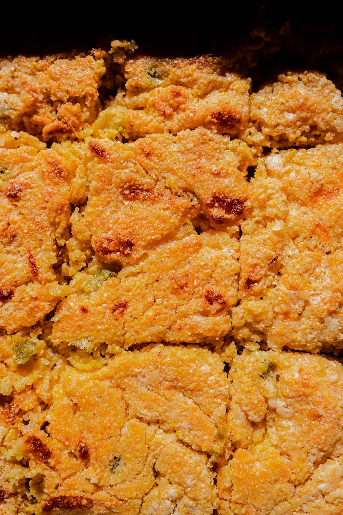 Close-up of golden-brown cornbread cut into squares, showing a crumbly texture and lightly browned, crispy edges.