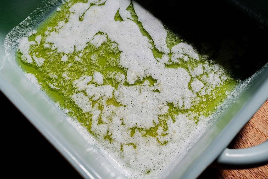 A close-up of melted butter with white foam on top in a light-colored baking dish.