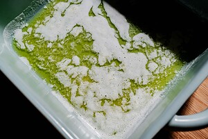 A close-up of melted butter with white foam on top in a light-colored baking dish.