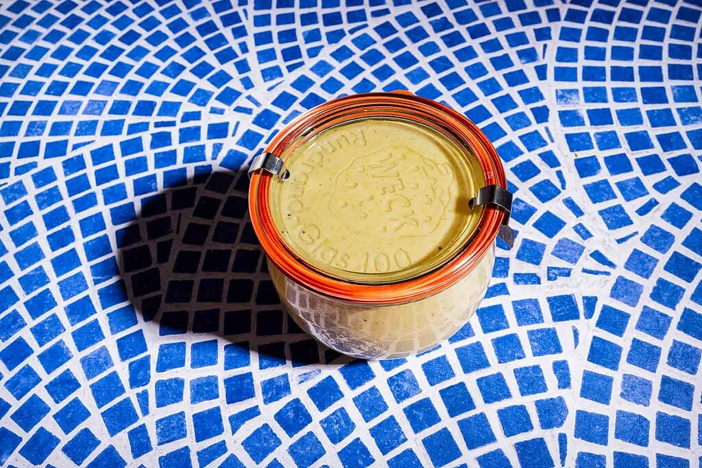A glass jar with an orange rubber seal and metal clasps, perfect for storing cabbage salad, sits on a blue and white mosaic tile surface.