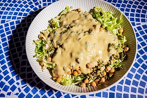 A bowl of chopped lettuce, cabbage salad, chickpeas, and seeds topped with a thick creamy dressing, placed on a blue and white patterned surface.