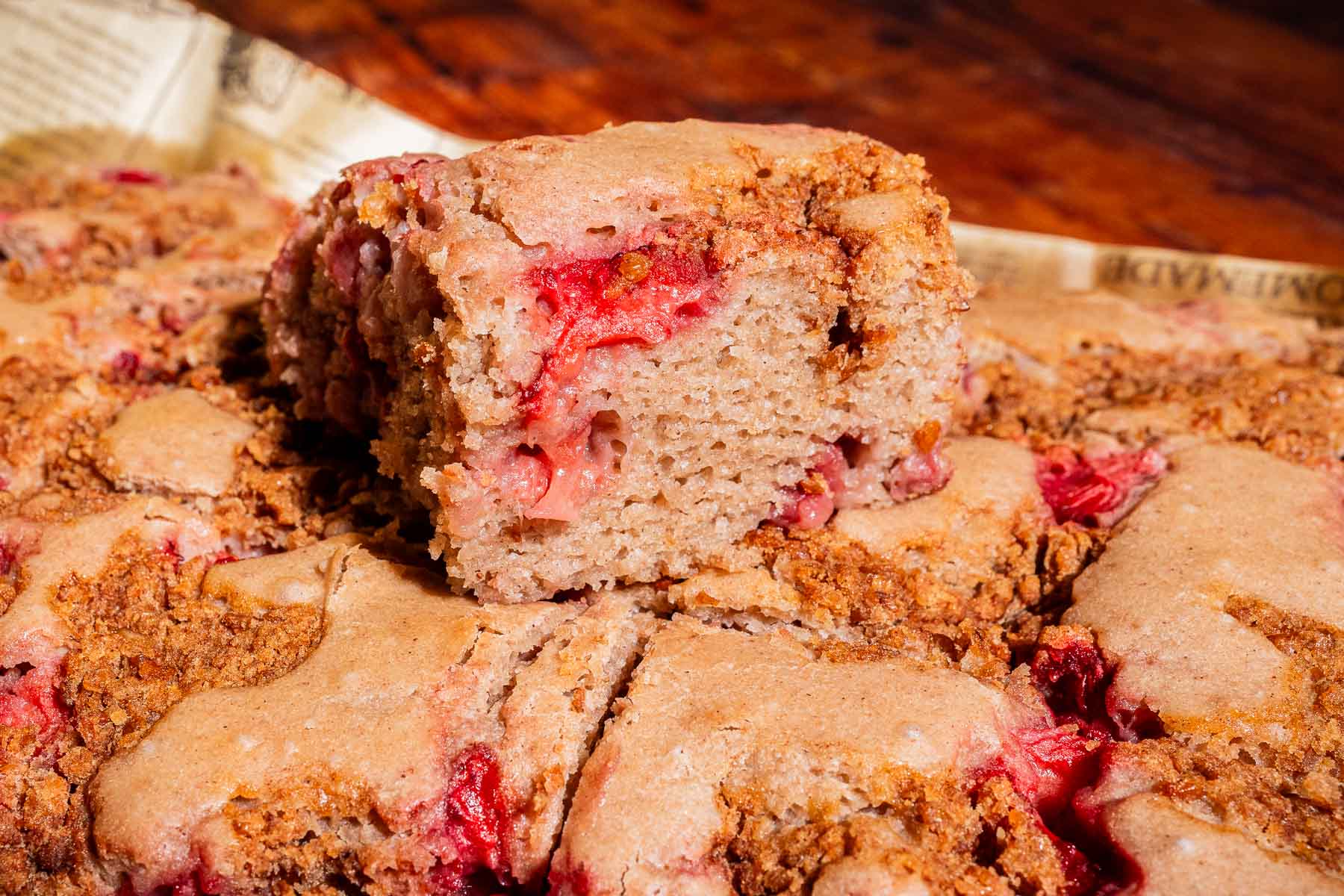 A close-up of a sliced strawberry buckwheat cake on parchment paper, with one square piece placed on top of the rest.