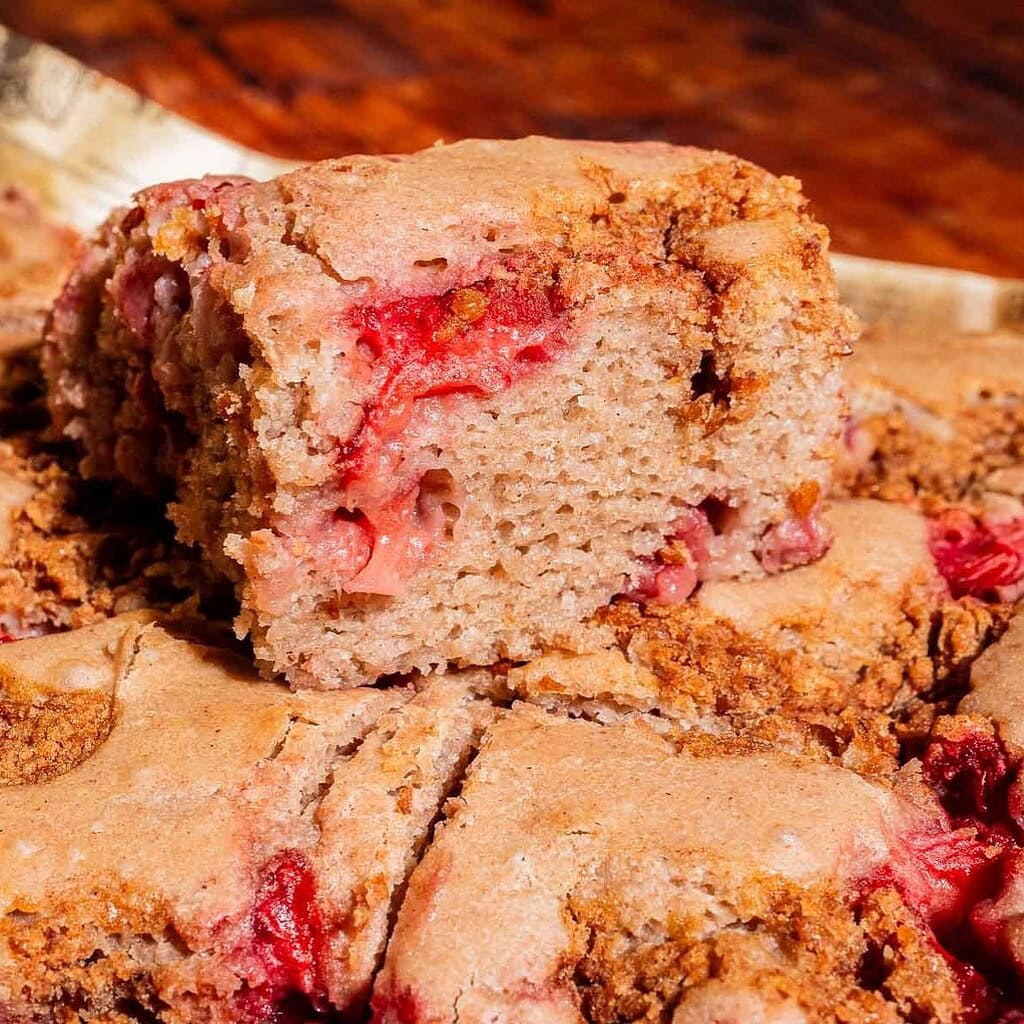 A close-up of a sliced, dense strawberry buckwheat cake with visible pieces of strawberries and a golden-brown crust.