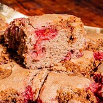 A close-up of a sliced, dense strawberry buckwheat cake with visible pieces of strawberries and a golden-brown crust.