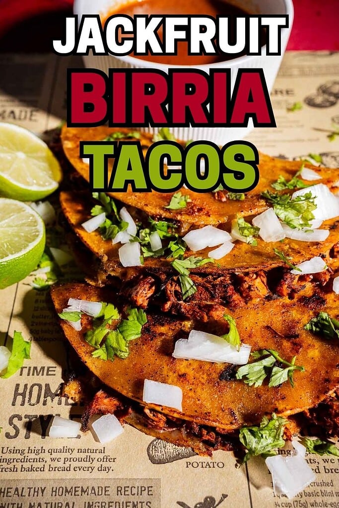 Three jackfruit birria tacos topped with chopped onions and cilantro, served with lime wedges and savory jackfruit birria broth, on a printed paper placemat.