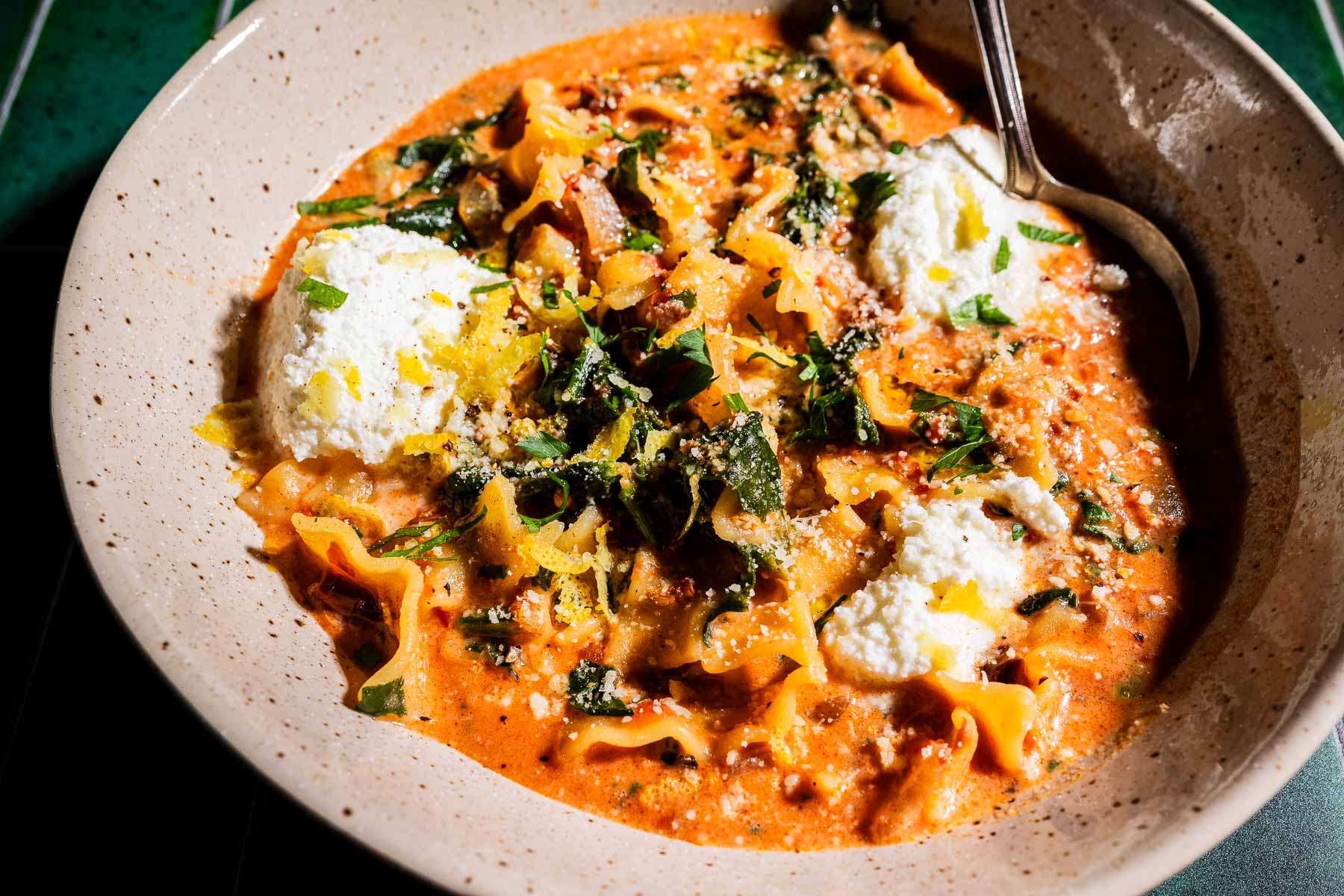 A bowl of creamy marry me lasagna soup, brimming with tomato broth, lasagna noodles, spinach, ricotta cheese, and fresh herbs, served with a spoon.