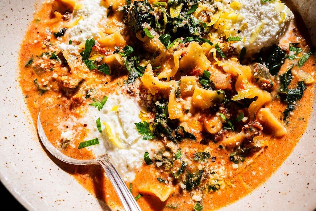 A bowl of marry me lasagna soup with pasta, tomato broth, spinach, ricotta cheese, and herbs, served with a spoon.